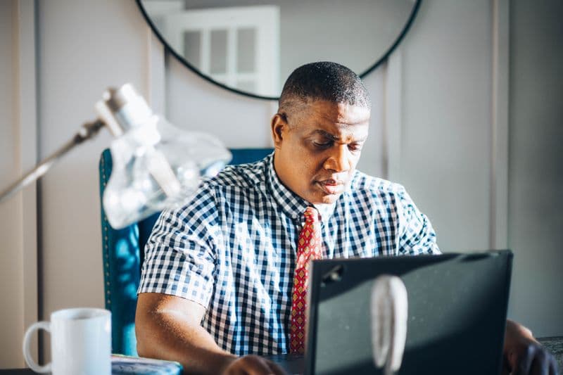 A concentrated adult man working on his laptop in a bright modern office setting.