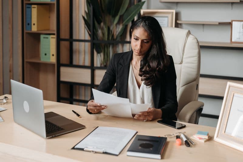 Business woman focused on paperwork at office desk, reviewing documents.