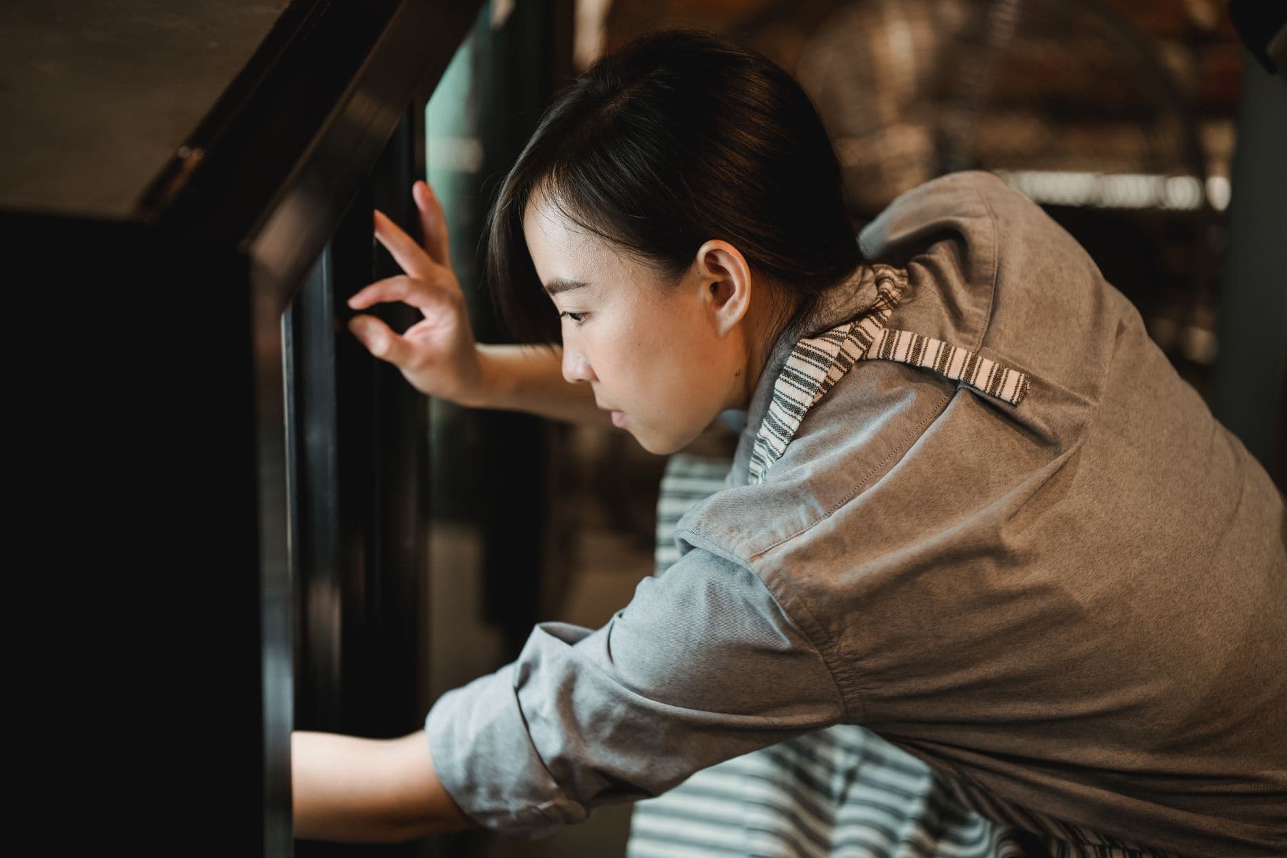 A waitress in a café apron, focused on inspecting an oven, showcasing attentive service.