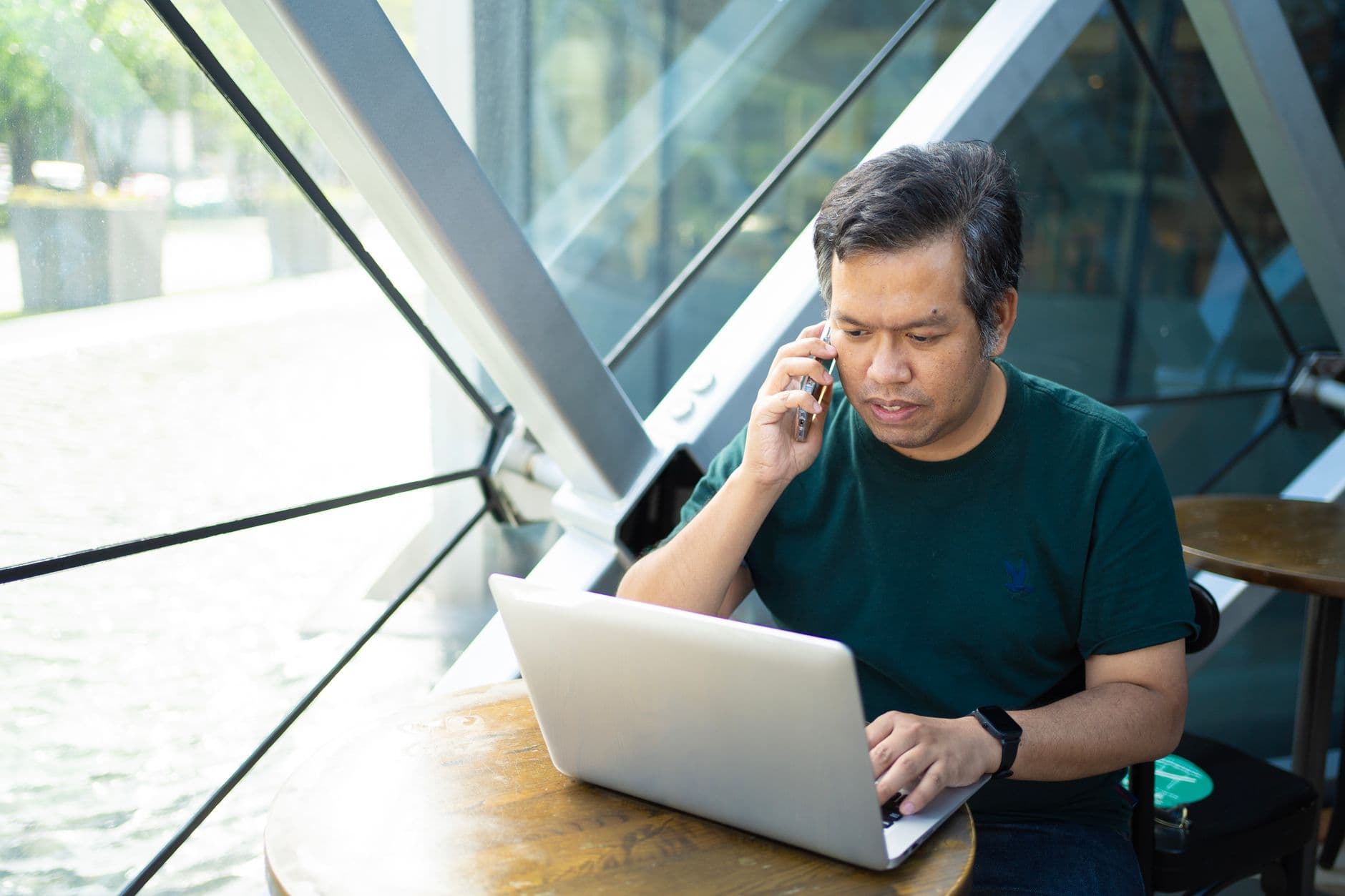 Asian man multitasking on laptop and phone in Bangkok café.
