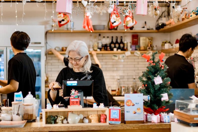 Elderly woman managing a festive cafe counter during Christmas season.