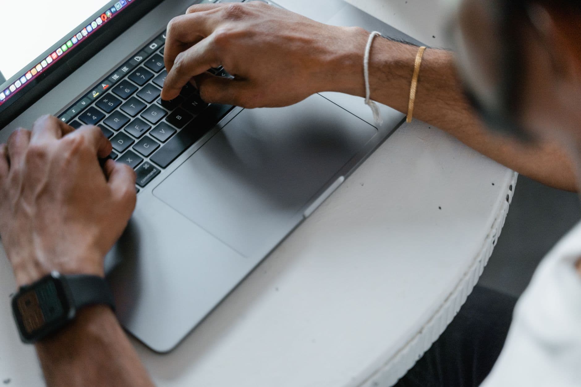 Hands wearing smartwatch and bracelet typing on a laptop keyboard.