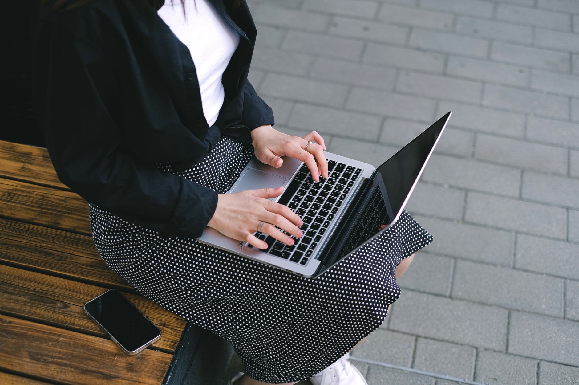 Woman sitting outdoors typing on a laptop, embodying freelance and digital nomad lifestyle.