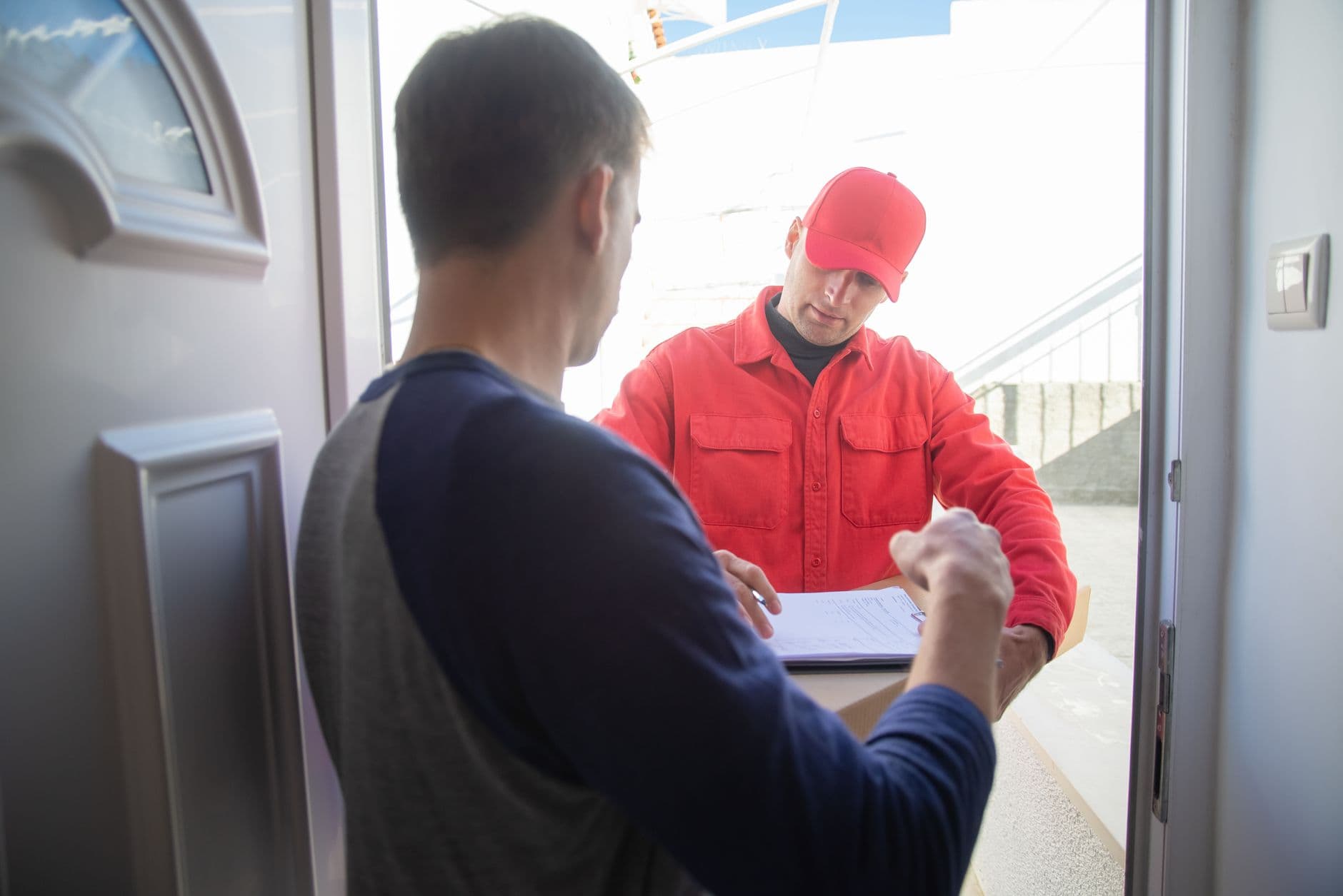 Courier in red uniform delivering a package at a customer's door in daylight.