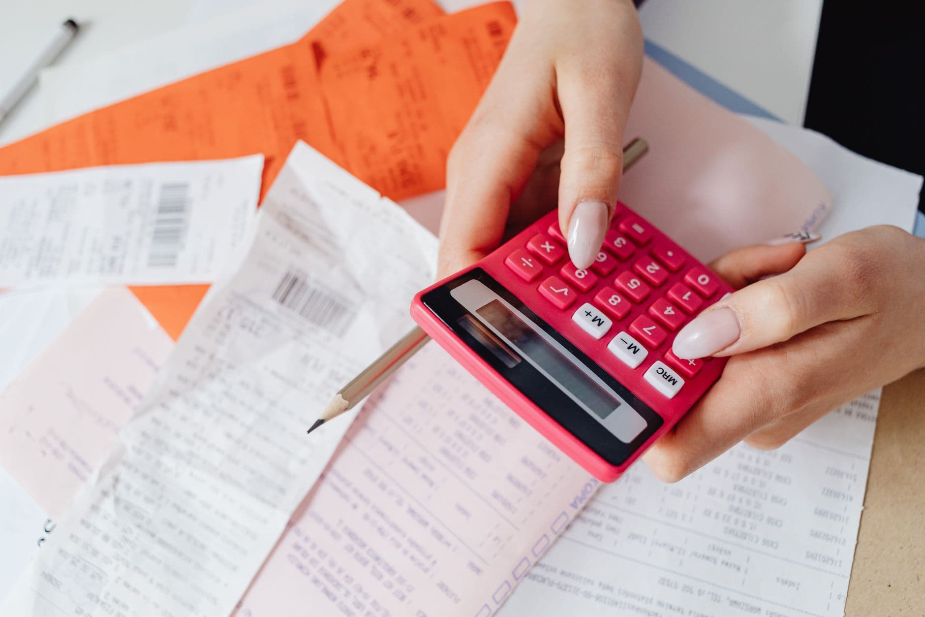 CBS no lugar de PIS e Cofins: o que muda no cálculo Hands using a pink calculator to manage expenses amidst various receipts and documents.