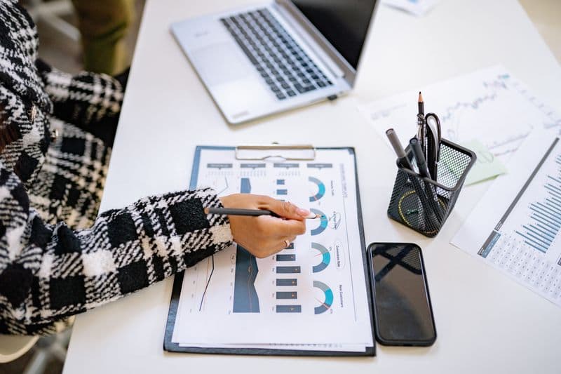 Certificado digital no celular: o que você consegue fazer An office setting with a person analyzing charts and graphs at a desk with a laptop and smartphone.