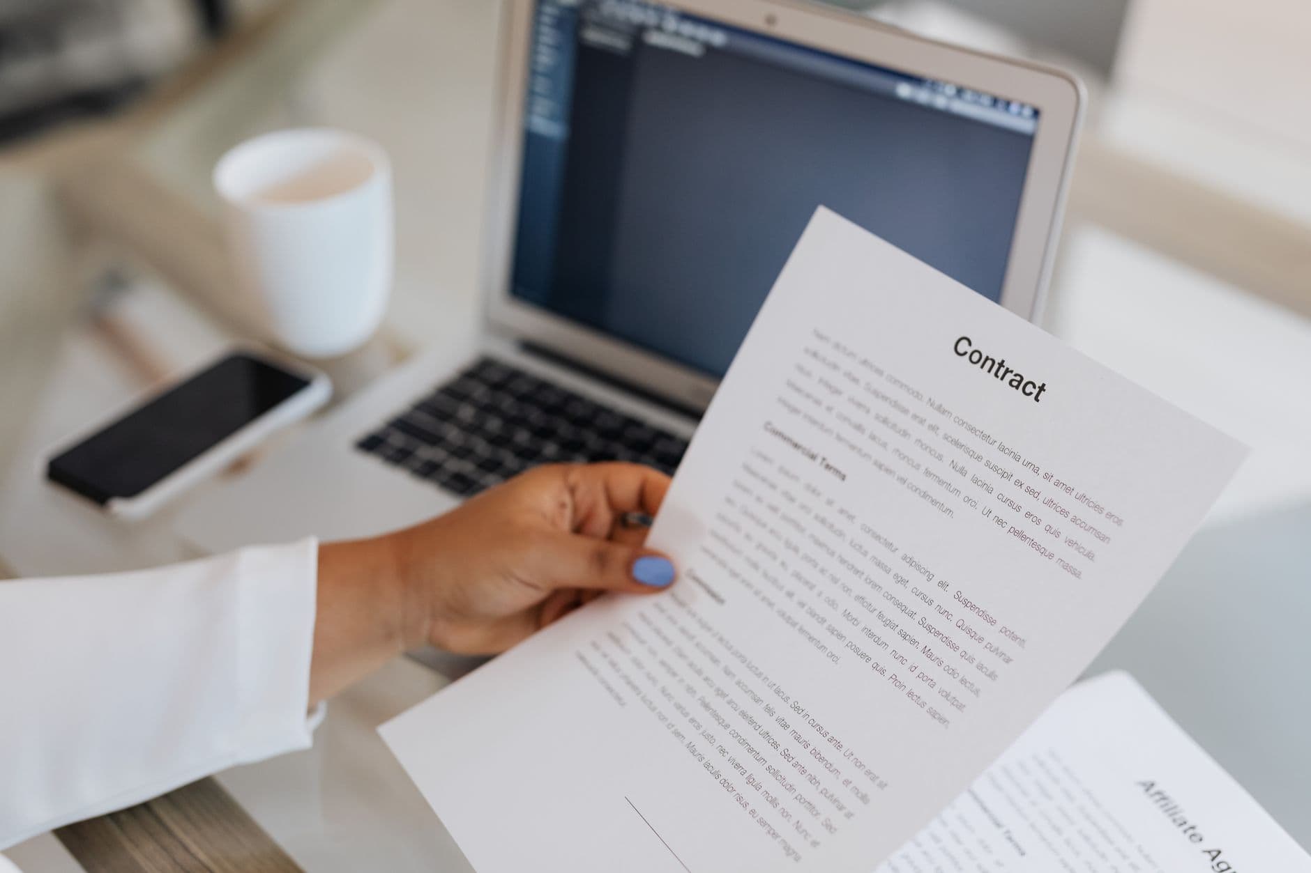 Certificado digital na nuvem: como funciona e quando usar Close-up of a person holding a contract document next to a laptop during a work session.