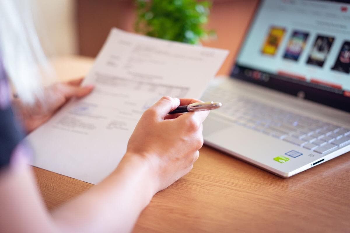 Mão segurando caneta perto do notebook, representando assinatura de documentos digitais