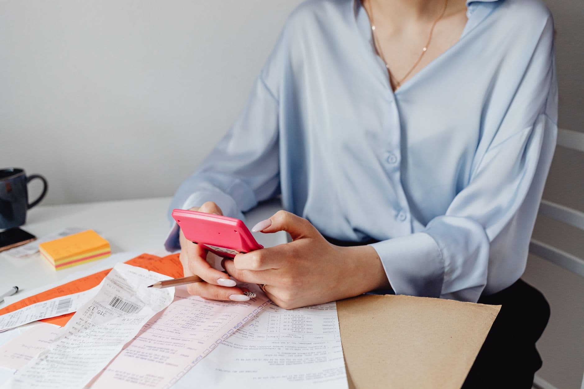 Emiti a nota e o cliente não pagou: o que fazer A woman using a pink calculator surrounded by bills and receipts at a desk.