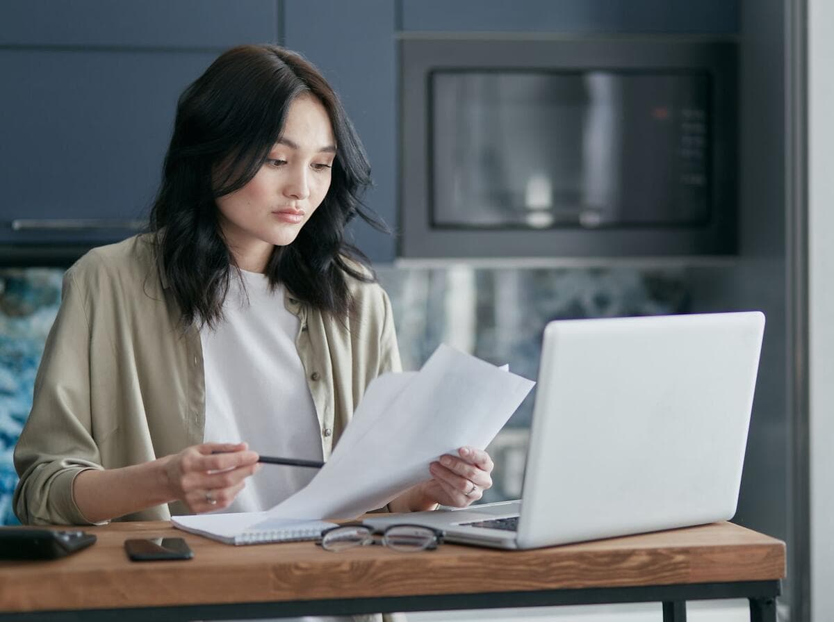 DAS em aberto e as dívidas do MEI Mulher revisando documentos e trabalhando no notebook em casa
