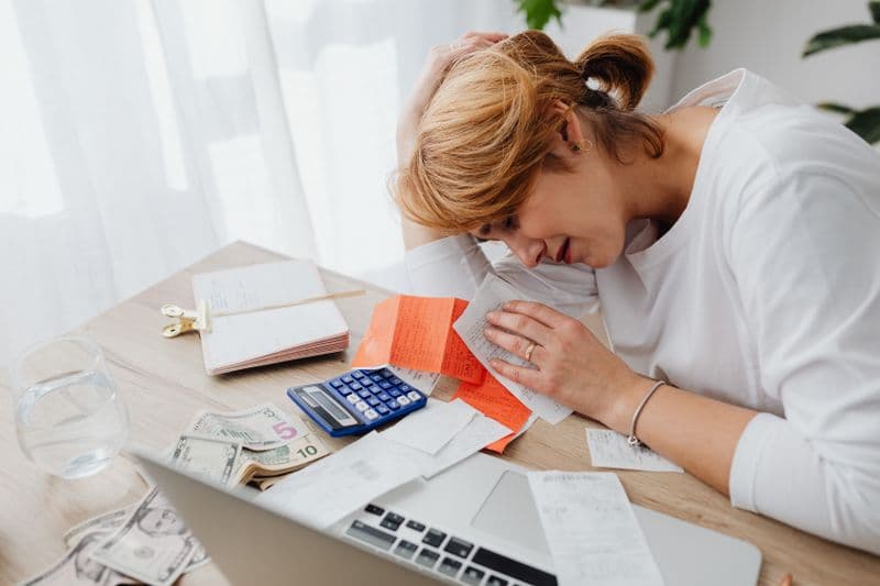 Como comprovar renda sendo MEI ou autônomo A woman overwhelmed with finances, surrounded by bills, calculator, and cash at home.