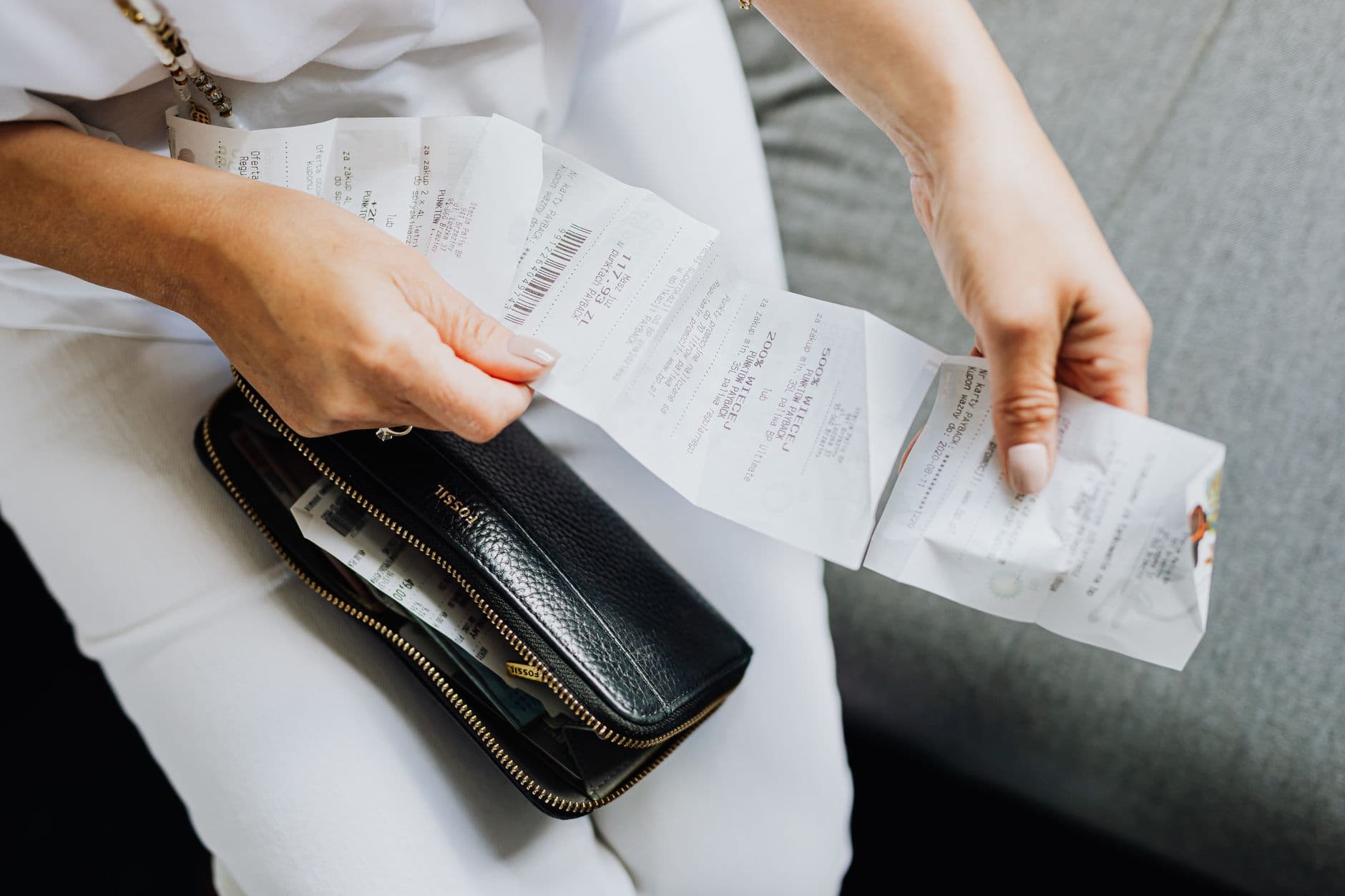 Como consultar nota fiscal eletrônica pela chave de acesso Close-up of a woman's hands managing multiple receipts taken from a black wallet.