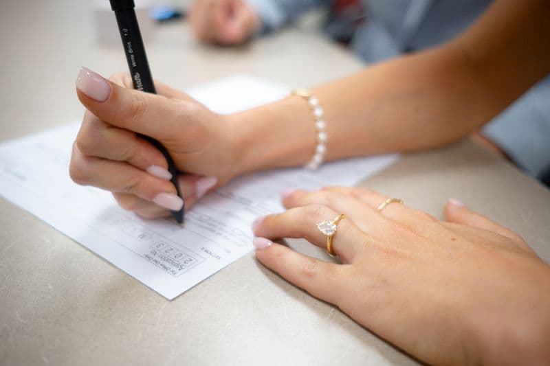 Posso abrir CNPJ no endereço da minha casa? Detailed view of hands filling out a form with elegant jewelry and manicure.
