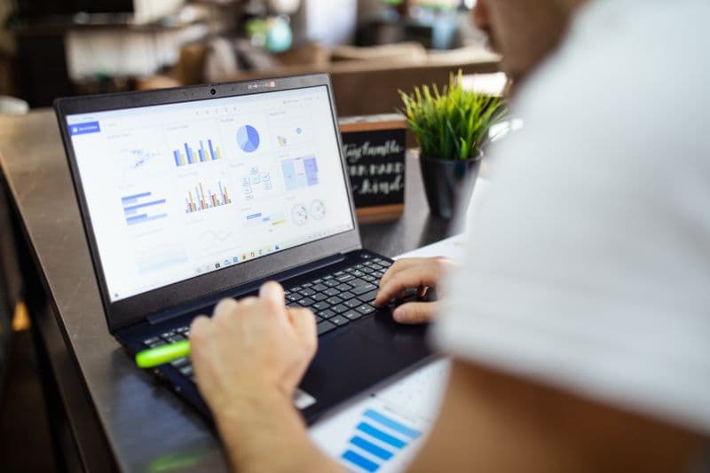 Fluxo de caixa para quem trabalha por conta própria Focused business analysis with charts and graphs on a laptop in a modern office setting.