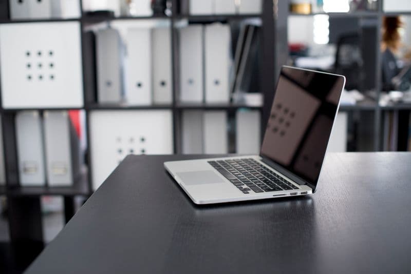 Por quanto tempo guardar as notas fiscais MacBook Pro displayed on a minimalist office desk with shelves in the background.