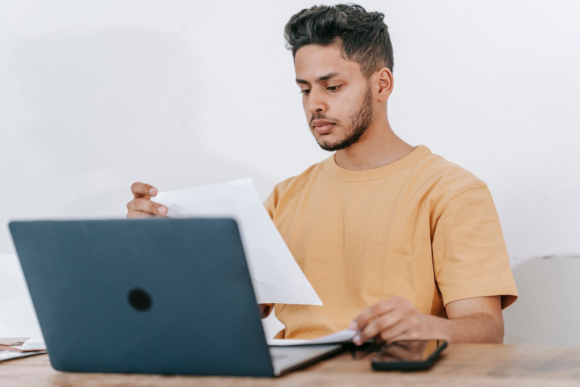 IBS e CBS: o que são e quem cobra Young bearded Hispanic male university student reading information on paper while studying online via laptop