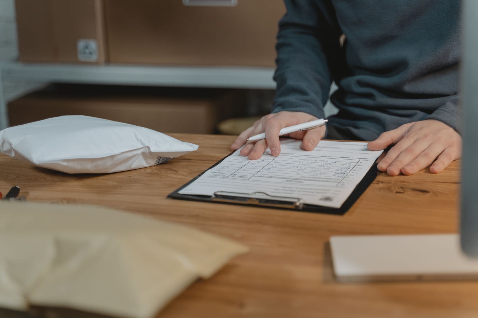 Preciso imprimir a nota fiscal? Entenda a regra Close-up of a person filling out a form on a clipboard with packages nearby in an office setting.