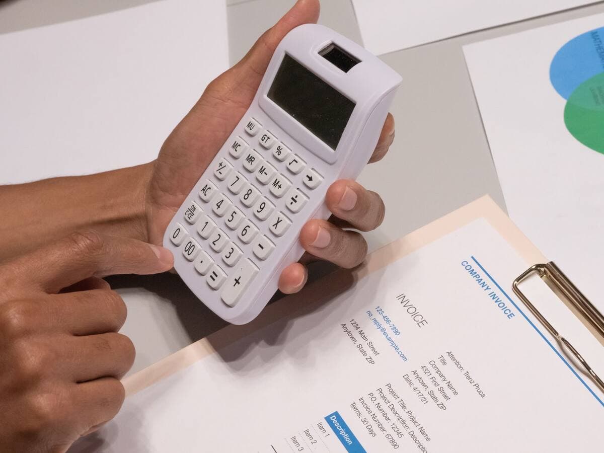 Mãos usando calculadora ao lado de uma nota fiscal de empresa