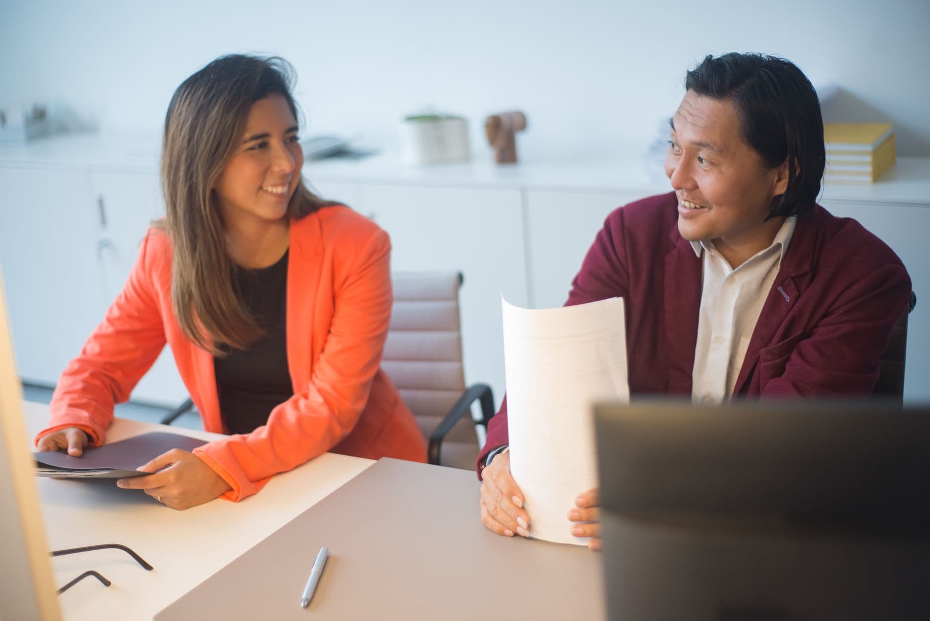 IVA dual brasileiro: entenda a divisão entre impostos Two business professionals smiling and discussing documents in a modern office.