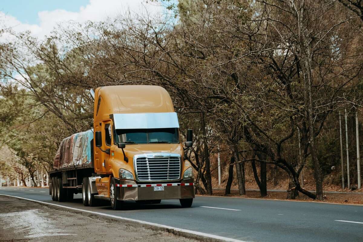 Caminhão de carga amarelo trafegando por uma estrada arborizada