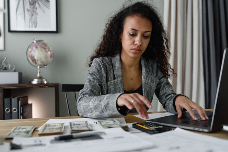 MEI com funcionário: o que muda nas obrigações Professional woman analyzing financial documents and counting cash at office desk.
