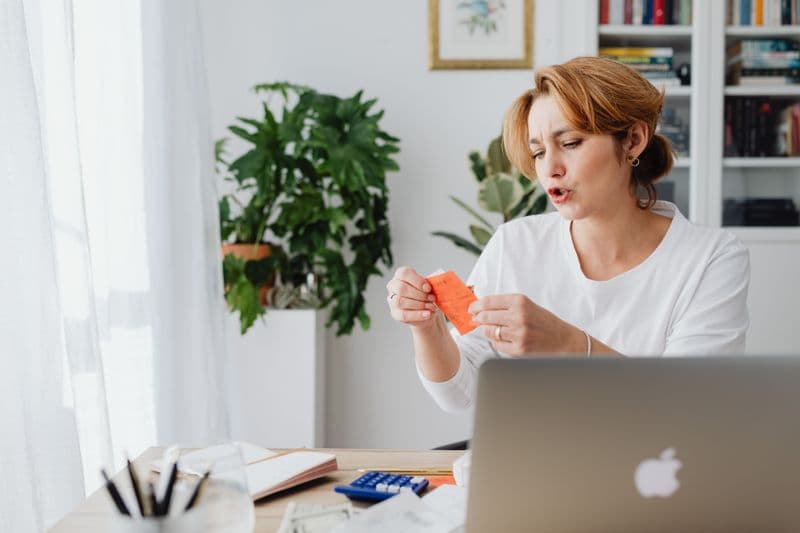 Estoureio limite do MEI: o que acontece com as notas Woman reviewing bills at home desk with laptop and plants, managing personal finances.