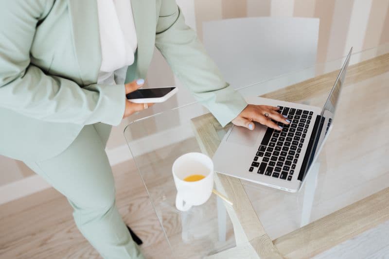 Emitir nota fiscal de MEI pelo celular: o que funciona A professional using a smartphone and laptop at a sleek glass desk in an office setting.