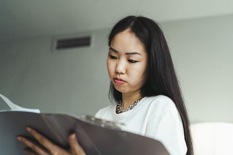MEI: uma nota por serviço ou uma nota por mês? Asian woman in casual attire examining paperwork with concentration indoors.
