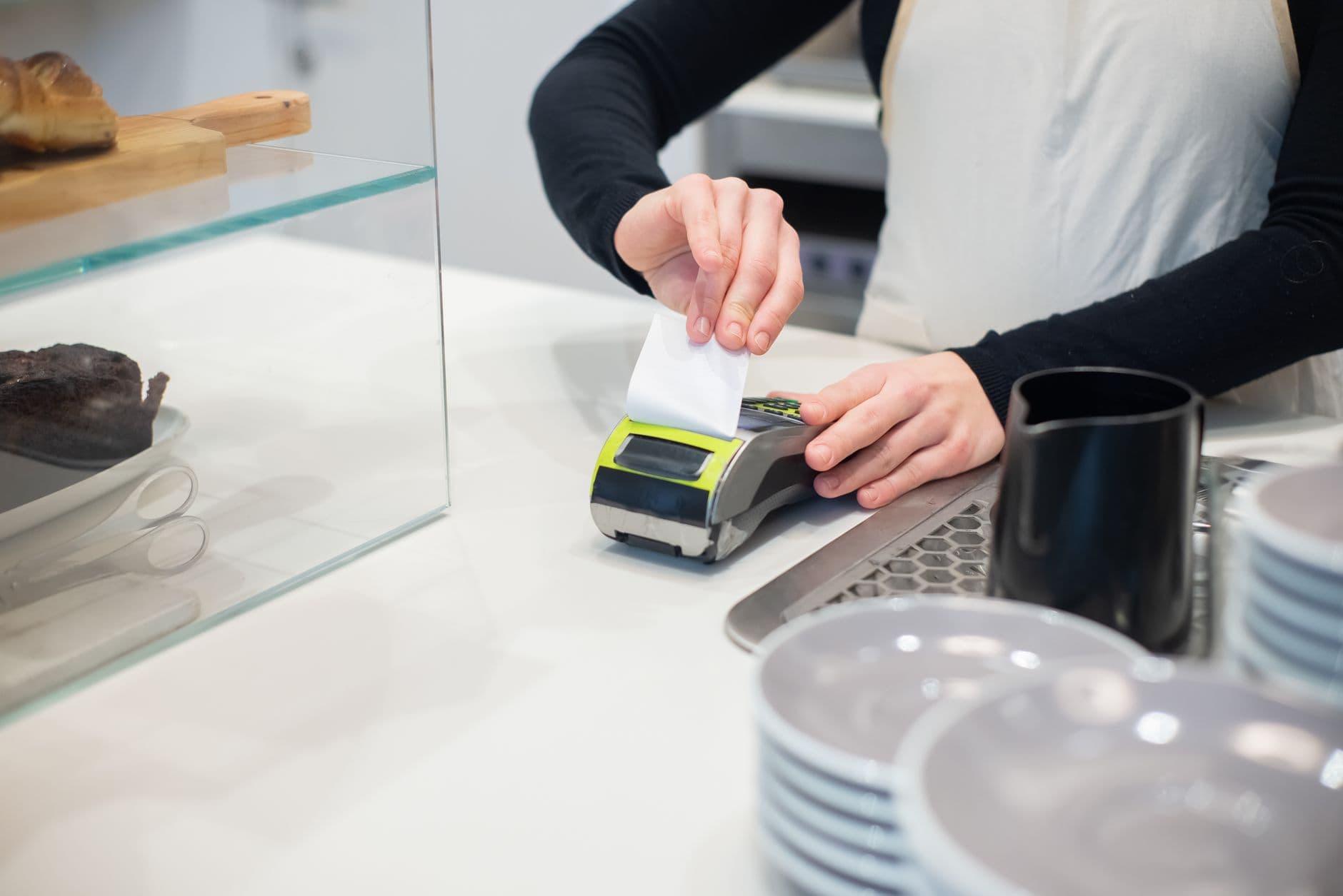 NF-e, NFC-e e NFS-e: qual o MEI usa Close-up of a cashless transaction at a modern café counter with hands holding a receipt.