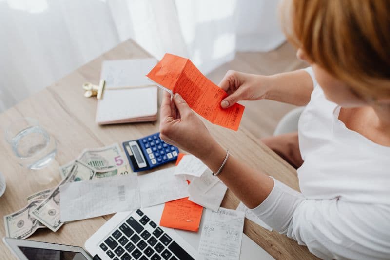 MEI: como emitir nota para órgão público sem devolução Woman using calculator and receipts at home office desk for finance management.