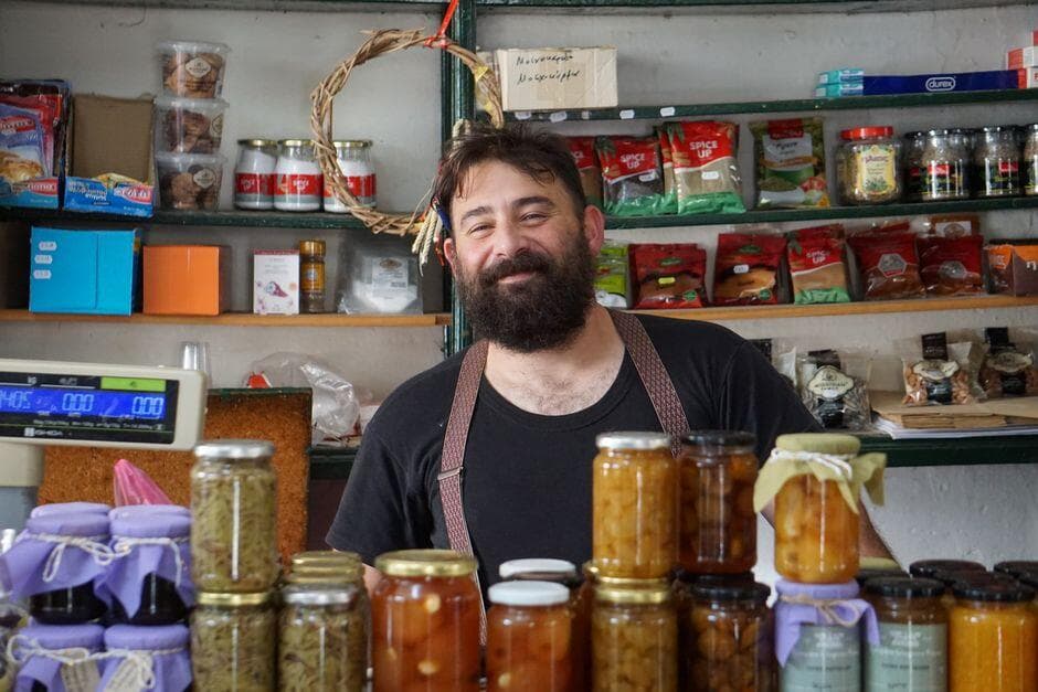 Comerciante sorridente atrás do balcão de uma loja com prateleiras de conservas
