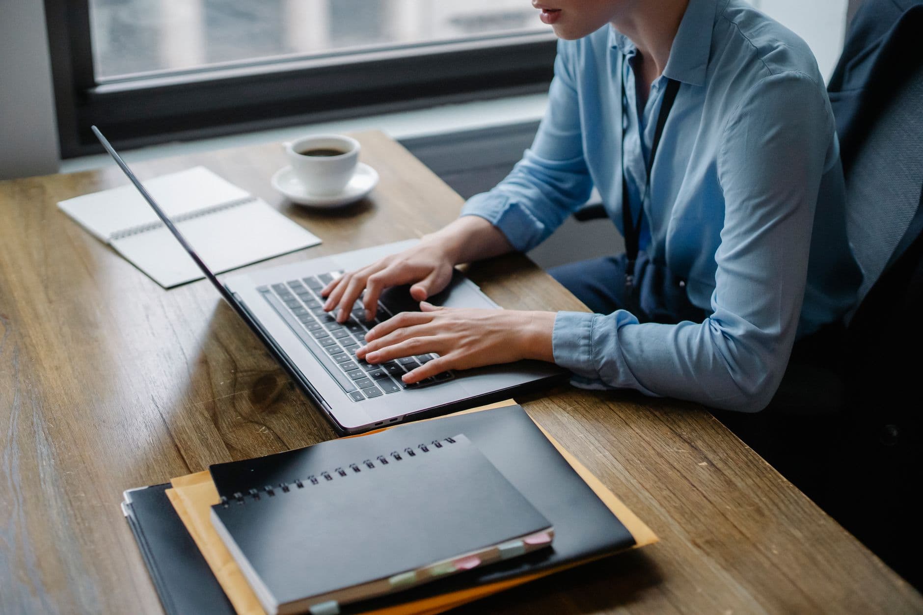 MEI não consegue emitir nota fiscal: causas e como resolver Office worker typing on laptop with coffee and notebooks on desk, capturing a focused work setting.