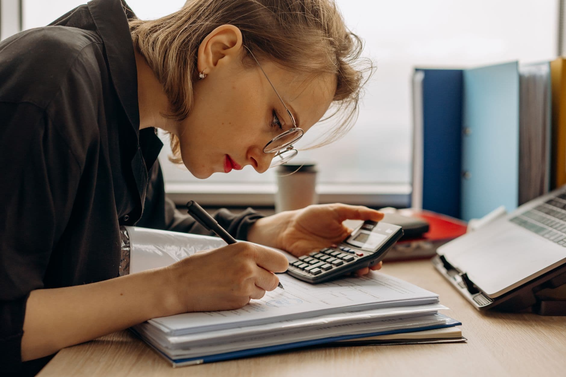 NFS-e no Simples Nacional: como preencher o ISS na nota Young woman diligently working on accounting with a calculator and documents. Perfect for business and finance themes.