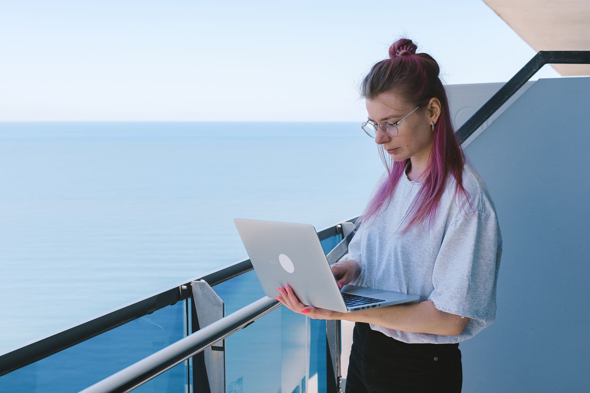 Como emitir NFS-e em Campo Largo A young woman works remotely on her laptop by the sea on a sunny day, embodying the digital nomad lifestyle.