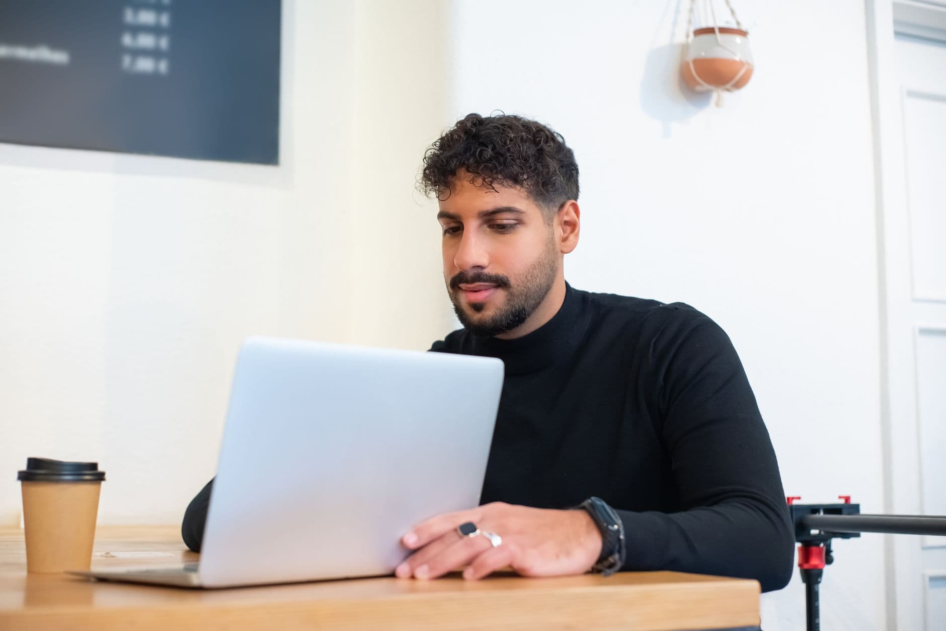 Nota Carioca: como emitir NFS-e no Rio de Janeiro Bearded man in a black sweater using a laptop in a contemporary office setting.