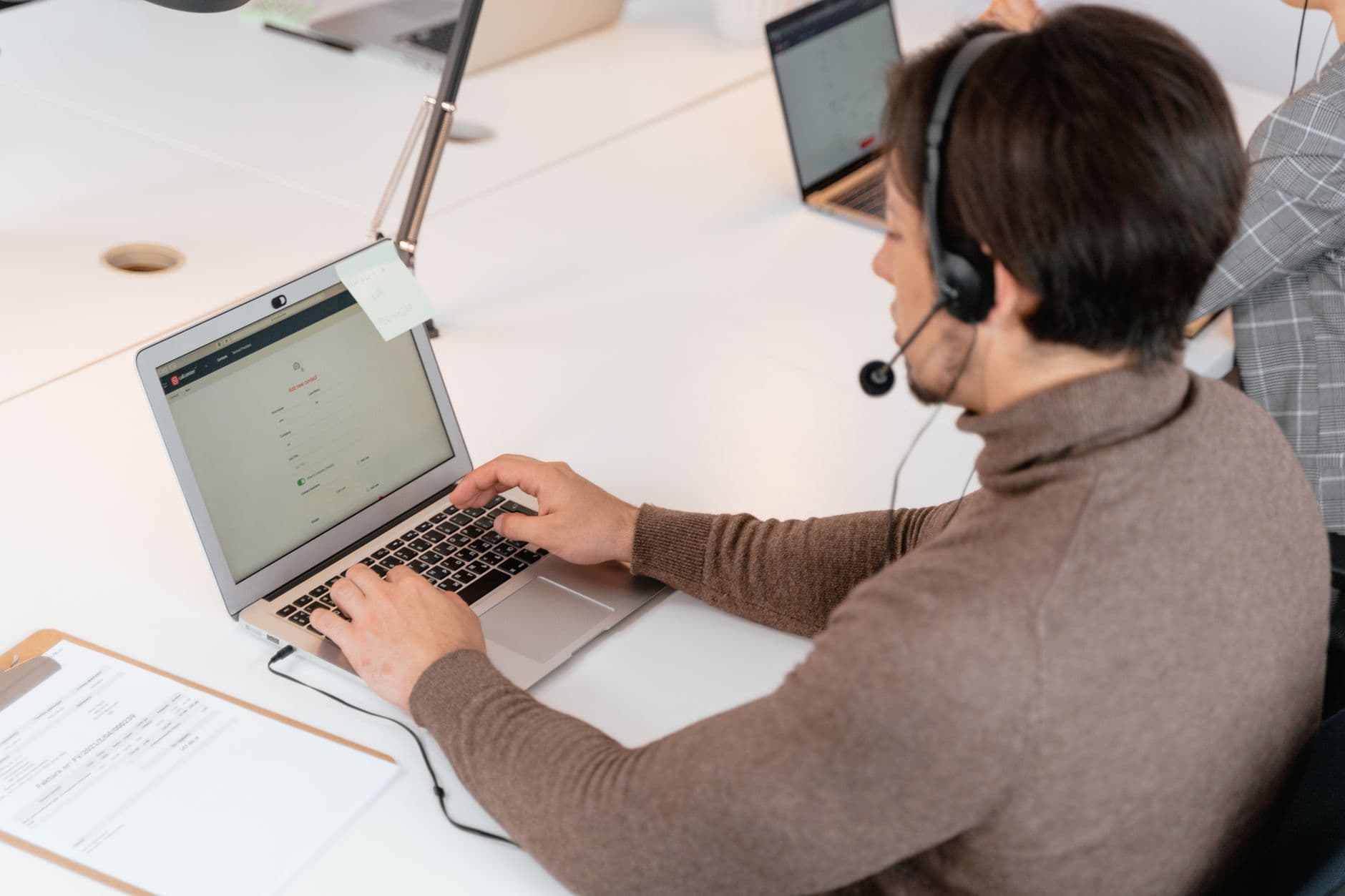 Nota Curitibana: como emitir NFS-e em Curitiba Call center agent wearing headphones working on a laptop in a modern office setting.