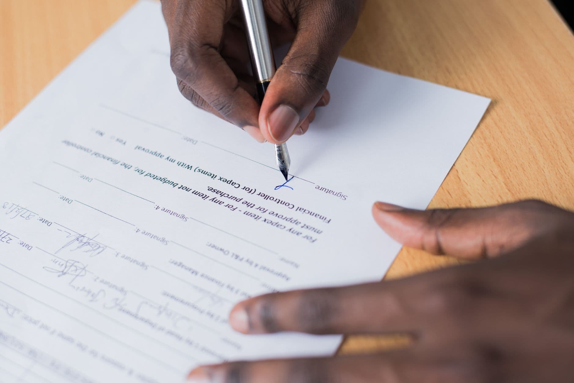 Nota fiscal na venda de ativo imobilizado A close-up view of a person's hand signing a business contract on a desk with a pen.