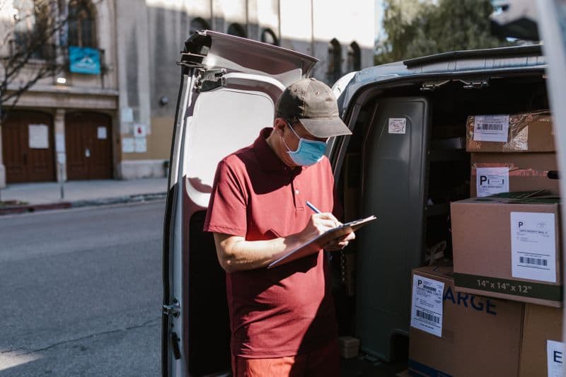 CFOP: como escolher o código certo da operação Courier with mask and clipboard arranging packages in delivery van.