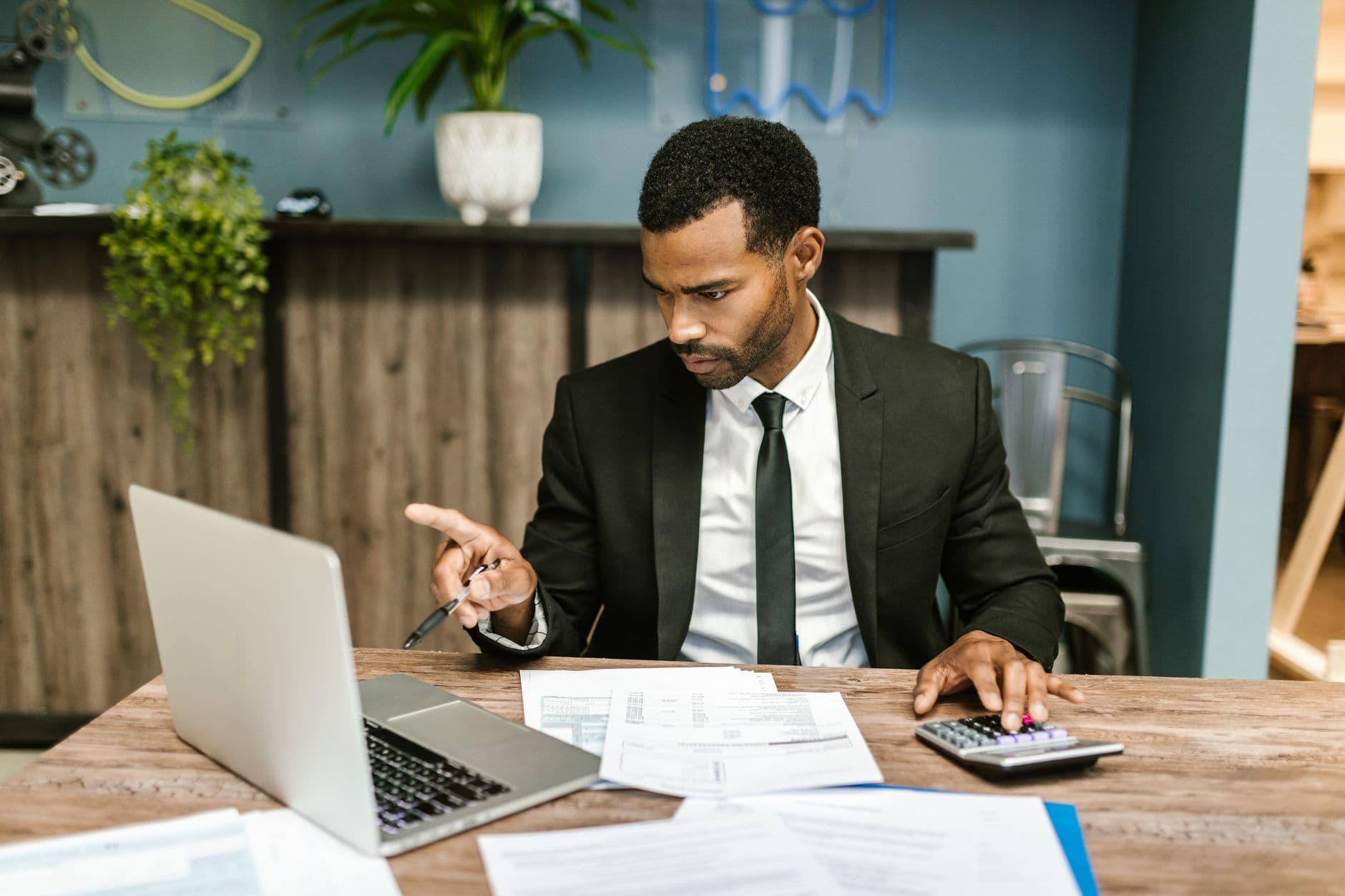 Nota fiscal complementar: para que serve e quando emitir Professional man in a suit using a laptop and calculator in an office setting.