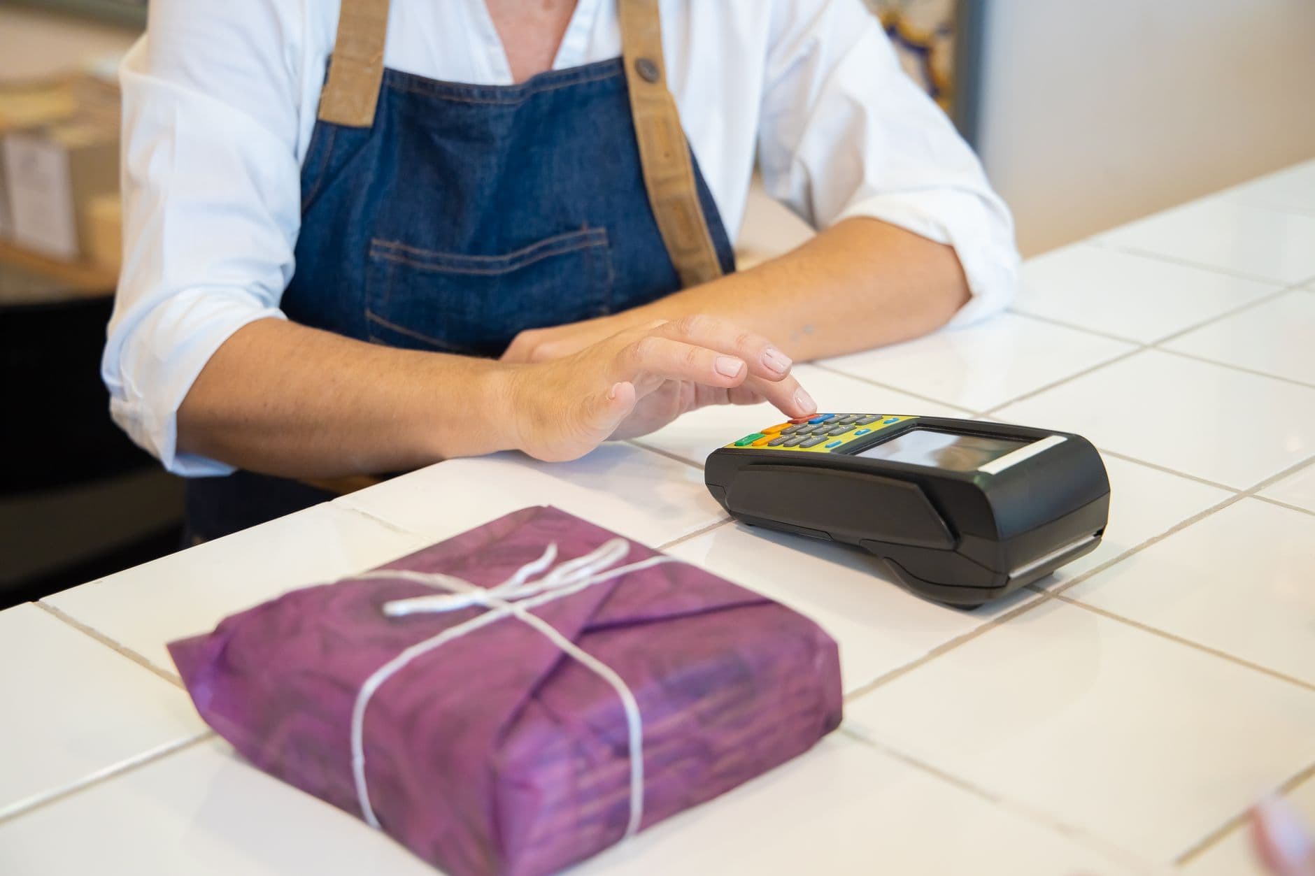 CPF na Nota e Cashback: O que Muda no Atendimento ao Cliente A person using contactless payment at a retail counter in Portugal wearing an apron.