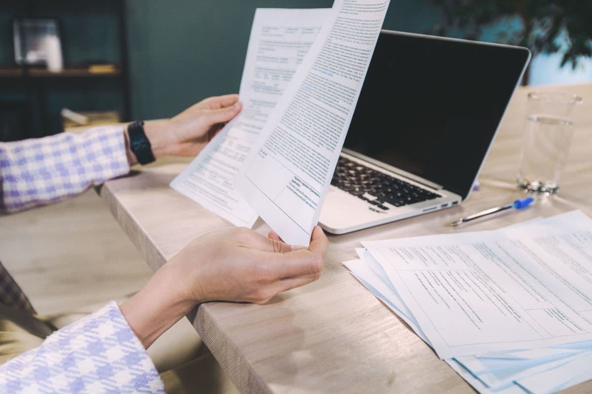 Pessoa responsável por um pequeno negócio revisando contratos e cobranças de clientes em uma mesa.