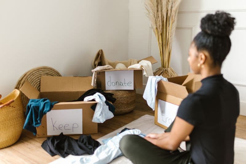 Nota fiscal de brinde, bonificação e doação A woman organizing clothes into labeled boxes for donation and keeping.