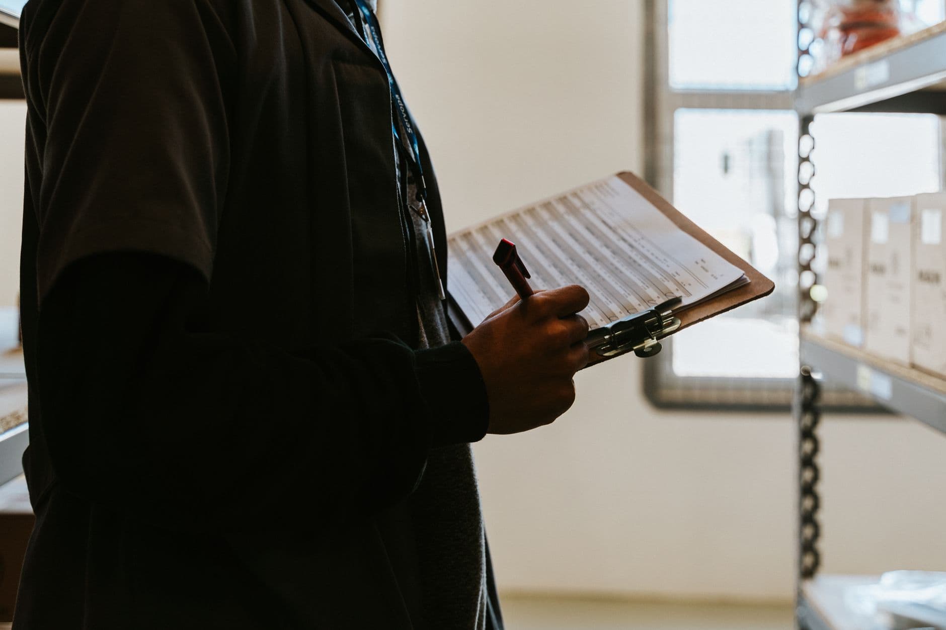 Nota fiscal de entrada: quando emitir para sua empresa Industrial worker managing inventory in a warehouse with a clipboard and checklist.