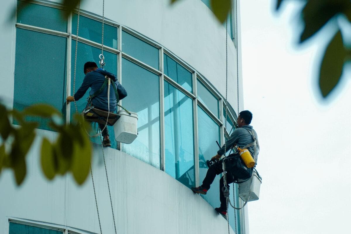 ISS retido: quando o condomínio desconta o imposto Equipe suspensa por cordas limpando os vidros da fachada de um prédio