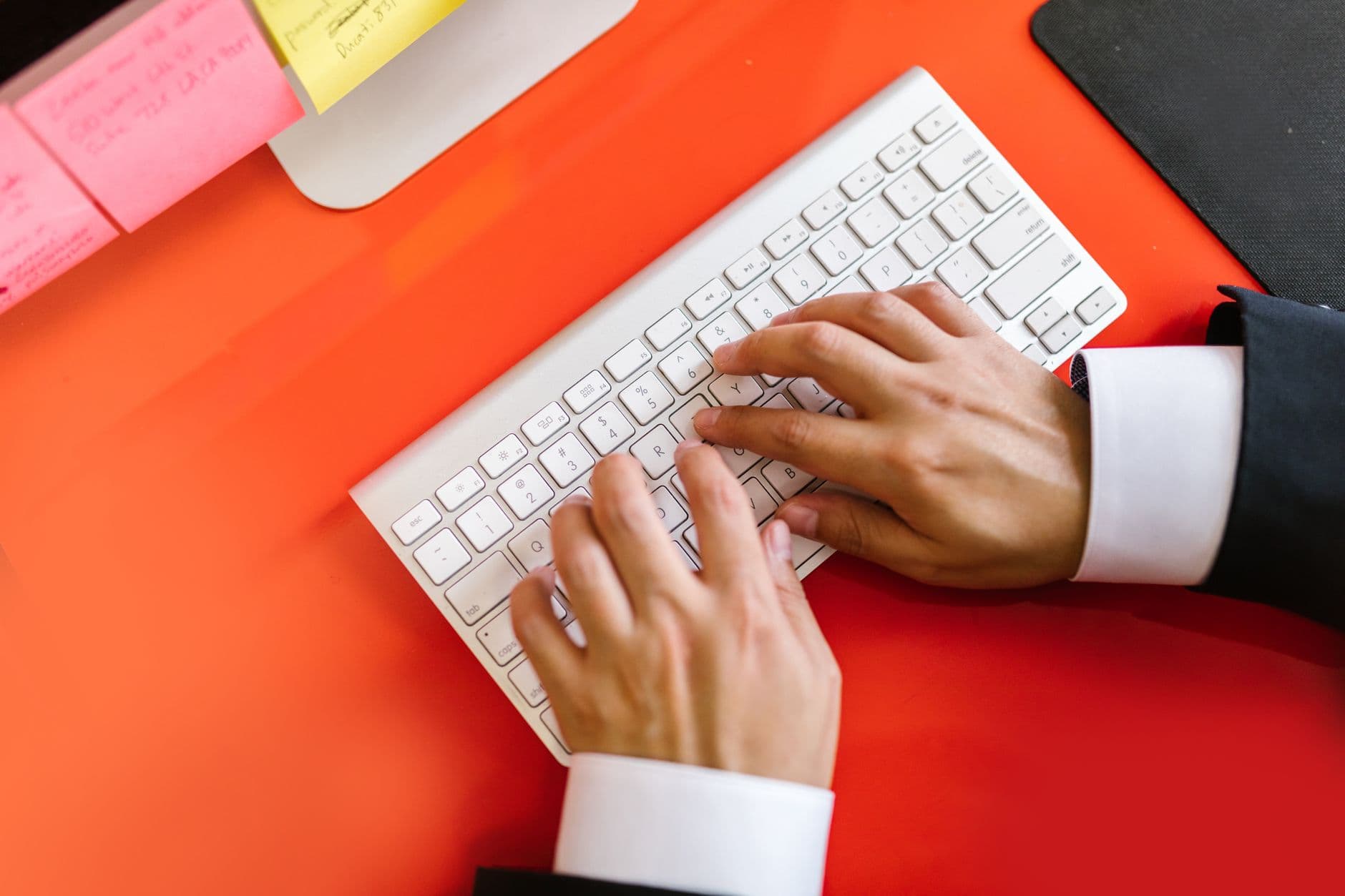Nota fiscal eletrônica em Ponta Grossa: como emitir NFS-e Close-up of hands typing on a wireless keyboard on an orange desk, ideal for tech and business themes.
