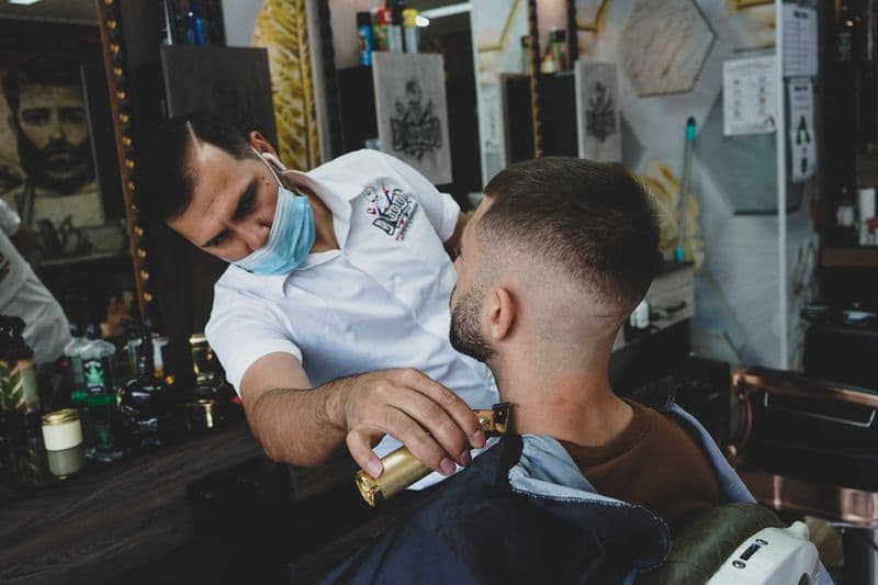 Nota fiscal para barbeiro: MEI, parceria e emissão Barber performing precise shaving with a razor on a client in a modern barbershop setting.