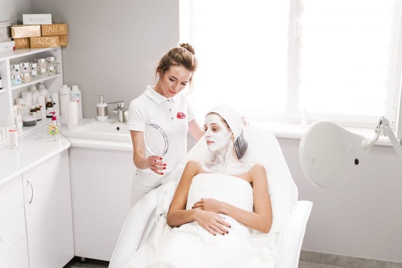 Nota fiscal para manicure, esteticista e profissionais de beleza Beautician applying a facial mask to a client in a modern salon. Professional skincare service indoors.