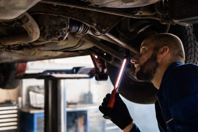Nota fiscal para mecânico autônomo: peças e serviços Mechanic using light to inspect vehicle undercarriage in workshop for maintenance.