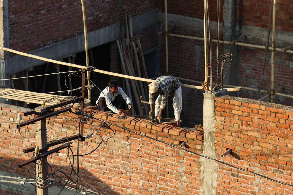 Dois pedreiros levantando uma parede de tijolos em uma obra ao sol