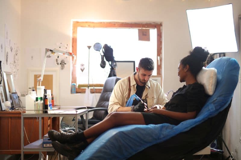 Nota fiscal para tatuador e estúdio: como emitir A tattoo artist working on a client's arm in a well-lit modern studio.